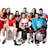 A group of eight young adults, each dressed in different sports uniforms, are posed together smiling. They hold various sports equipment including a soccer ball, volleyball, basketball, football, tennis racket, and table tennis paddle. The clothing includes jerseys and gear for soccer, hockey, football, and other sports. The background is plain white, emphasizing the colorful attire of the group.