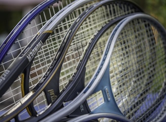 Several tennis rackets are closely positioned together, showcasing their strings and frames. The rackets have various colors and branding, including visible text on some frames.