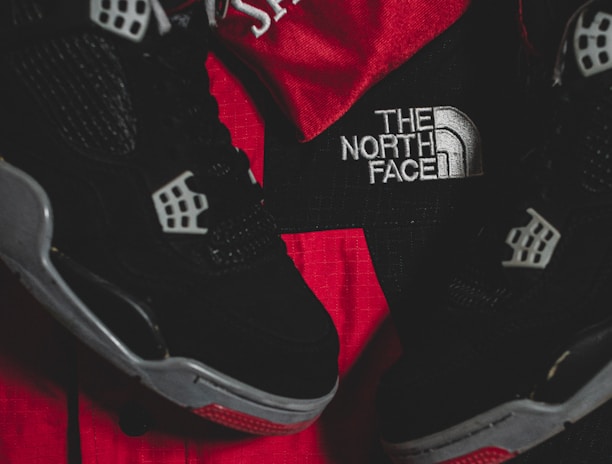 Black athletic shoes are placed alongside red and black sportswear bearing logos from Spalding and The North Face.