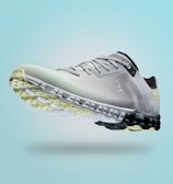 A single sports shoe is prominently displayed against a seamless, light turquoise background. The shoe features a sleek design with a gradient of light gray to dark gray tones, and is equipped with a distinctive CloudTec sole for cushioning. The branding logo is subtly visible on the side.