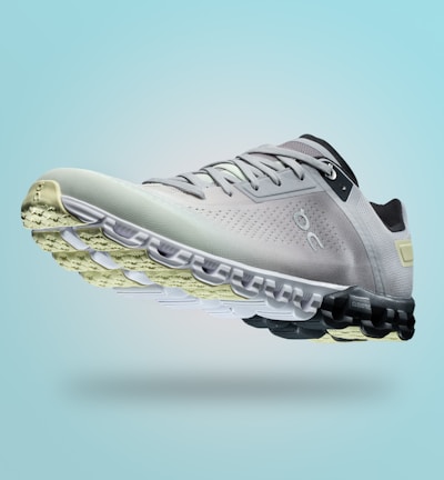 A single sports shoe is prominently displayed against a seamless, light turquoise background. The shoe features a sleek design with a gradient of light gray to dark gray tones, and is equipped with a distinctive CloudTec sole for cushioning. The branding logo is subtly visible on the side.